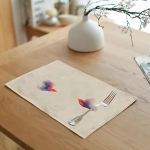 Detailed macro of a linen placemat with watercolor hummingbird prints on a wooden table.
