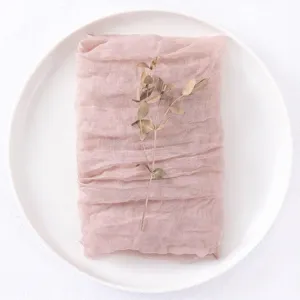 Rustic blush pink gauze cheesecloth table napkin folded neatly on a white ceramic plate