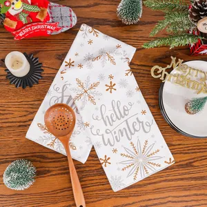 Close-up of white Christmas kitchen towels featuring gold snowflake prints and Hello Winter text