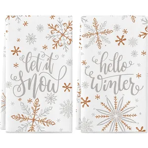 Pair of white Christmas kitchen towels featuring gold snowflake prints and winter greetings