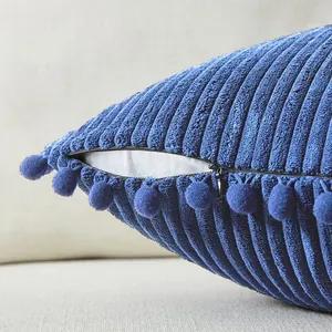 Vista detallada de una funda de cojín de pana azul con pompones decorativos y cremallera oculta.