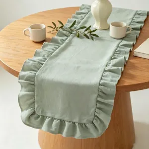Détail d'un chemin de table en lin vert sauge avec d'élégants bords à volants.