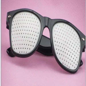 Detail shot of black frame pinhole glasses presented on a pink textured background