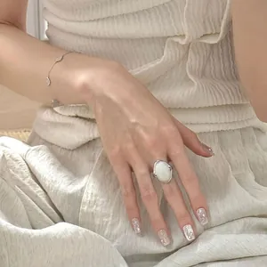 Nahaufnahme eines luxuriösen, übergroßen ovalen Rings mit weißem Edelstein am Finger