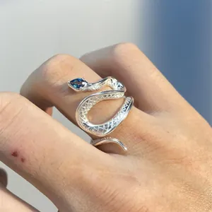 Close-up detail of a silver snake ring featuring a blue teardrop gemstone on a finger.