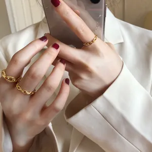 Detailed close-up of a minimalist chunky gold chain link ring worn with a white blazer.