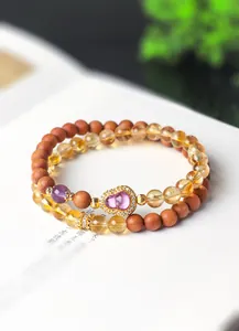 Close-up van dubbelstrengs armband met citrienkralen, sandelhout en amethist kalebas bedel
