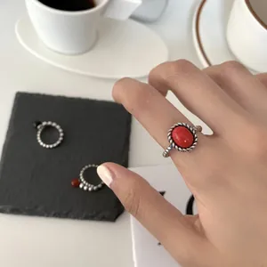 Close-up of a 925 silver braided ring with a red oval gemstone worn on a finger.