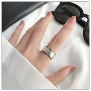 Close-up of wide silver ring with polished surface and beaded edges worn on index finger.