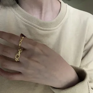 Detailed view of gold chain and pig nose rings on hand with beige knitwear background.