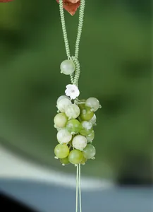 Detail of green chalcedony grape ornament with elegant braided cord and white flower.