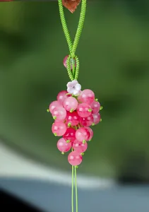 Detailed view of a pink chalcedony grape-shaped pendant with a green woven cord.