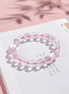 Gros plan d'un bracelet en perles de cristal rose naturel posé sur un livre ouvert.