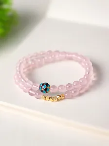 Primer plano de una elegante pulsera de cuarzo rosa con una cuenta de esmalte floral única.