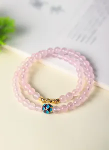 Vista detallada de una pulsera de cuarzo rosa con cuenta de esmalte azul y detalles dorados.