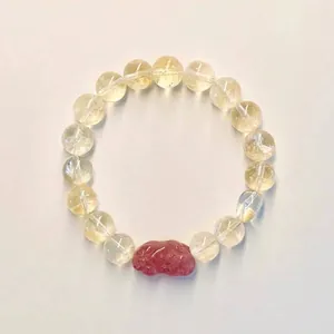 Vue détaillée d'un bracelet en citrine jaune avec un charm en quartz fraise rouge