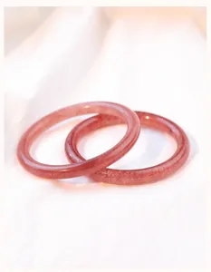 Detailopname van twee natuurlijke roze aardbeikwarts kristallen armbanden op witte stof.