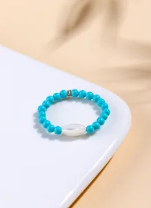 Detailed macro view of a turquoise beaded ring with a center white shell bead on a plate