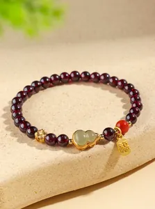 Vue détaillée d'un bracelet en perles de grenat avec un charme Wu Lou en jade Hetian et un tag Fu.