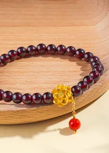 Gros plan d'un bracelet en perles de grenat rouge foncé avec un délicat charm de lotus doré.