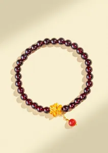 Gros plan d'un bracelet en perles de grenat rouge foncé avec un charm fleur en or délicat.
