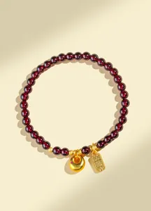 Détail d'un bracelet en perles de grenat naturel avec des breloques dorées porte-bonheur