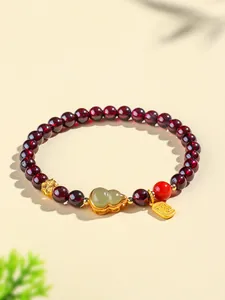 Gros plan d'un bracelet en perles de grenat avec une gourde en jade et charme doré