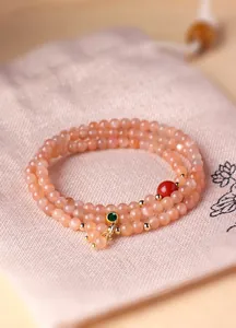 Detailopname van een elegante meerlaagse armband van perzik zonnesteen met smaragdgroene bedel