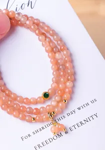 Gedetailleerde close-up van een perzik zonnesteen kralenarmband met meerdere strengen en hanger