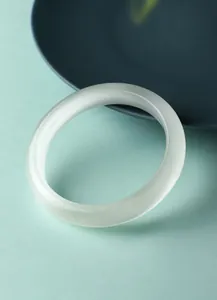 Detailopname van een witte kattenoogsteen armband met chatoyance-effect op groene achtergrond