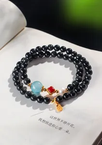 Gros plan d'un bracelet à deux rangs en perles noires avec un charm de gourde dorée.