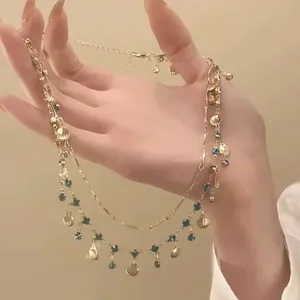 Detail van de dubbellaagse gouden ketting met schelphangers en blauwe gems