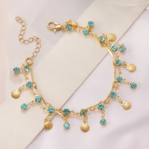 Detail van gouden dubbellaagse ketting met blauwe kristallen en kleine schelphangers