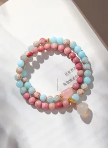 Detailaufnahme eines Armbands aus rosa Rhodonit und blauem Achat auf Papier