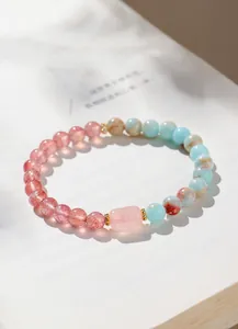 Nahaufnahme eines Perlenarmbandes aus Erdbeerquarz und Rosenquarz auf einem weißen Buch.