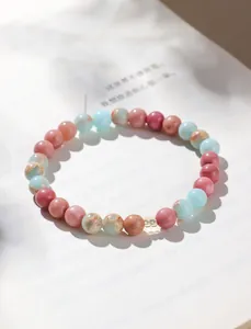 Nahaufnahme von rosa und blauem Natursteinperlenarmband auf weißem Buchhintergrund