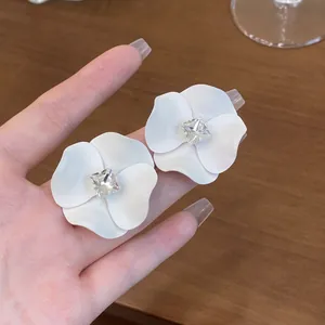 Primo piano di eleganti orecchini a fiore bianco opaco con zircone quadrato centrale