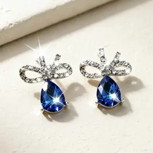 Dettaglio orecchini a goccia blu con fiocco di strass argentati per feste eleganti