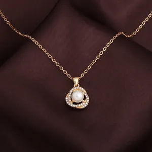 Primo piano di una collana dorata con ciondolo di perla incastonato di cristalli.