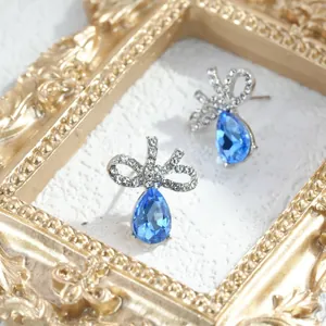 Dettaglio di orecchini a fiocco in argento con cristallo a goccia blu e strass chiari.
