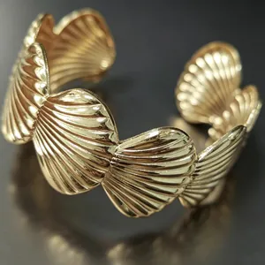 Dettaglio di un elegante bracciale rigido dorato con motivo a conchiglia e finitura lucida