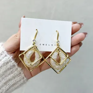 Dettaglio di eleganti orecchini geometrici dorati con pendente a goccia in maglia.