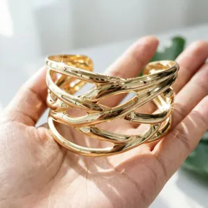 Dettaglio di un ampio bracciale rigido dorato geometrico traforato sulla mano calda