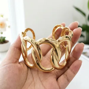 Primo piano di un bracciale a polsino in oro a maglie grandi, finitura lucida oro.