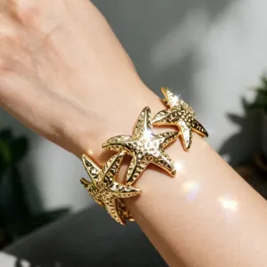 Vista dettagliata di un elegante bracciale largo regolabile con stelle marine d'oro su un polso