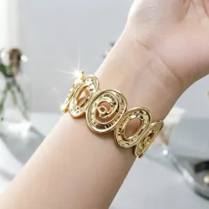 Dettaglio di un elegante bracciale a fascia dorato con spirali geometriche sul polso