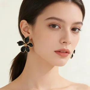 Eleganti orecchini a fiore minimalisti in smalto nero con bordo dorato su una modella