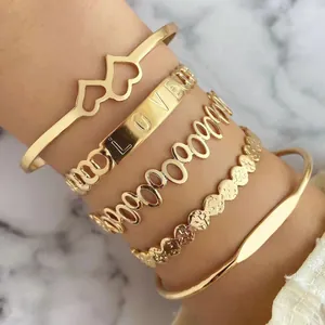 Dettaglio macro di bracciali rigidi dorati con incisione LOVE e motivi a cuore