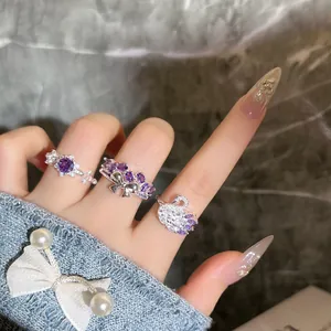 Gros plan de bagues en argent avec pierres violettes, motifs cygne et nœud.