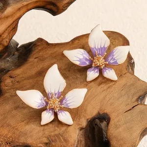 Dettaglio orecchini in smalto a forma di fiore a cinque petali viola sfumato su legno.